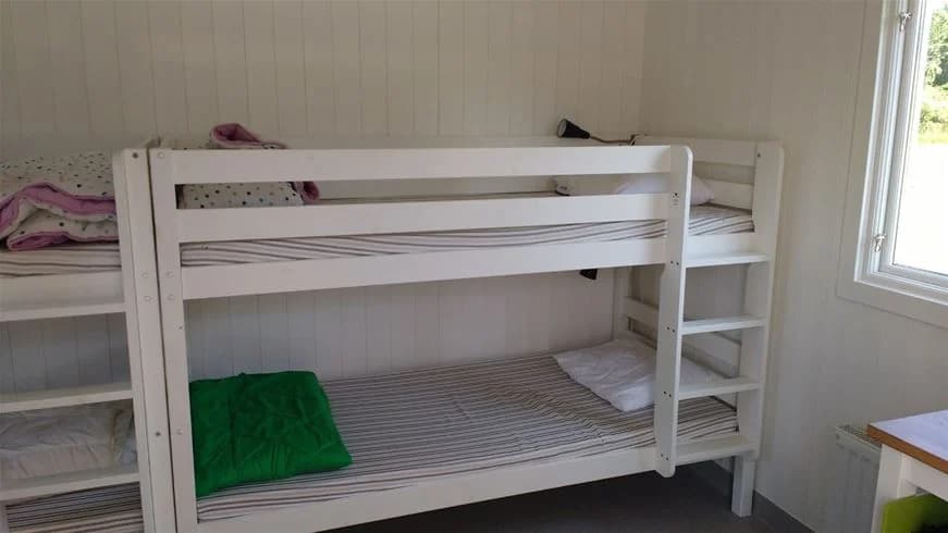 En våningssäng i ett sovrum med trägolv och träinredning, bäddad med vita lakan och omgiven av enkel och avskalad inredning typisk för en campingmiljö.