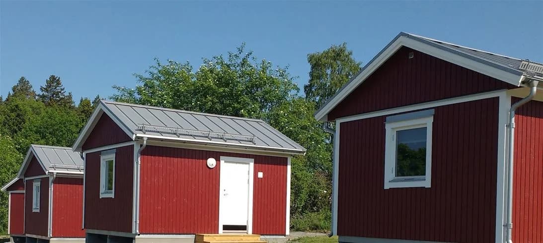 En bild av flera små stugor och trädgårdsbyggnader på Norrtälje Camping, omgivna av grön gräsmatta och träd.