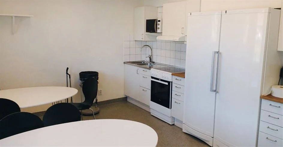 Bild av en modern och välutrustad inomhusmiljö på Norrtälje Camping. Rummet har trägolv och ljus träinredning, inklusive köksdel med vitvaror och arbetsbänk.