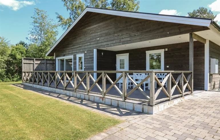 En trästuga med veranda på Norje Boke Camping, omgiven av gröna omgivningar, perfekt för en naturnära vistelse.