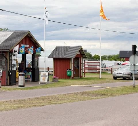 En campingplats med gemensamt utrymme under tak, bänkar och bord för avkoppling nära skuggiga träd.