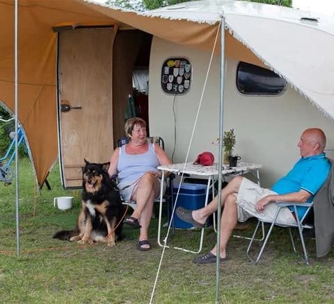En solig campingplats med tält och utemöbler, inklusive en hopfällbar stol, som skapar en inbjudande och avslappnad stämning på Neptuni Camping.