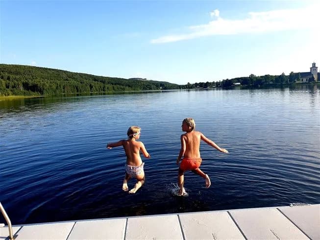 En grupp människor njuter av fritidsaktiviteter vid en vacker sjö under sommaren, omgiven av grönska och lugn natur.