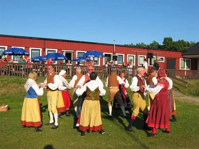 En grupp människor deltar i traditionella dans- och underhållningsaktiviteter i en utomhusmiljö på Möllstorps camping. Färgglada kläder och en festlig atmosfär förstärker känslan av gemenskap och glädje.