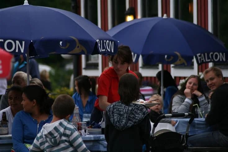 En livlig campingplats med många människor under parasoller, som njuter av ledig tid och avkoppling i solstolar. 