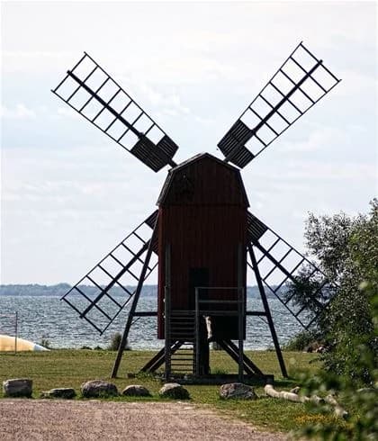 En väderkvarn står på en grön grässlätt vid Möllstorps camping, omgiven av vidsträckt landskap.