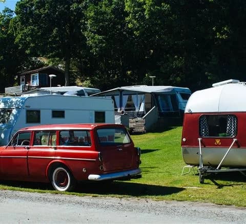 En klassisk bil parkerad på Marstrands familjecamping, synlig med bakluckan, stötfångaren och registreringsskylten. Bakom bilen skymtar fler fordon och campingmiljö.