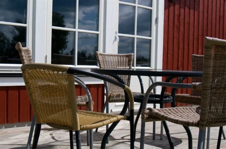 En bild av en bekväm utegrupp vid Mjölknabbens camping, med flätade stolar och ett träbord på en uteplats.