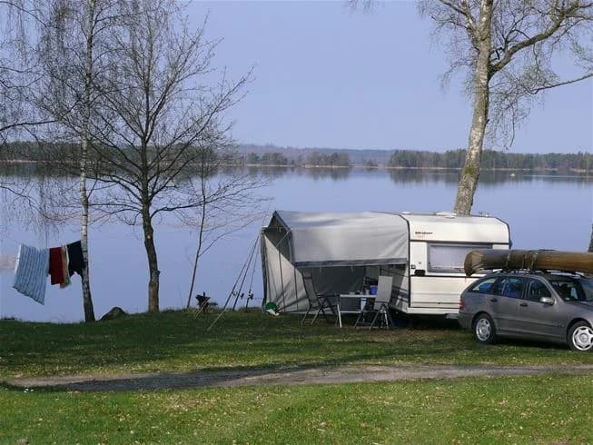 En naturskön campingplats vid en sjö med tält och husvagnar, omgiven av grönska och vatten.