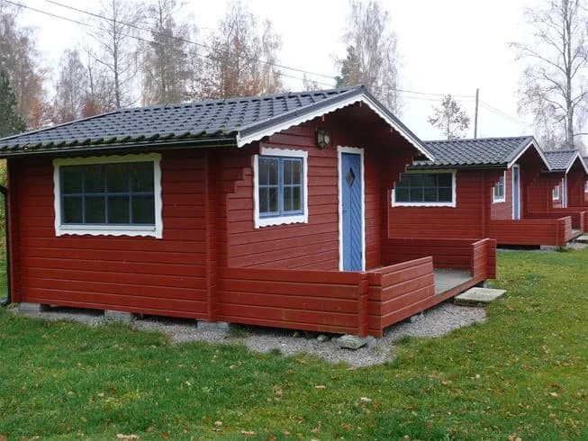 En trädstuga med träfasad och plåttak vid Mjölknabbens camping, omgiven av grönskande natur.