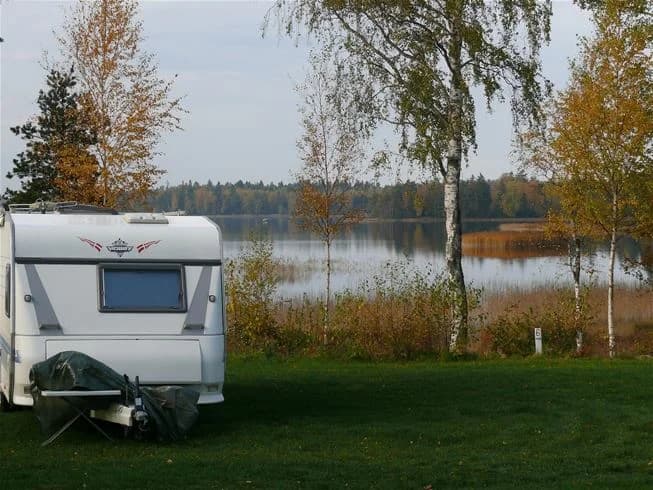 En caravan och en husbil står parkerade vid Mjölknabbens camping, omgiven av en naturskön miljö med en sjö i bakgrunden och frodig vegetation runtom.