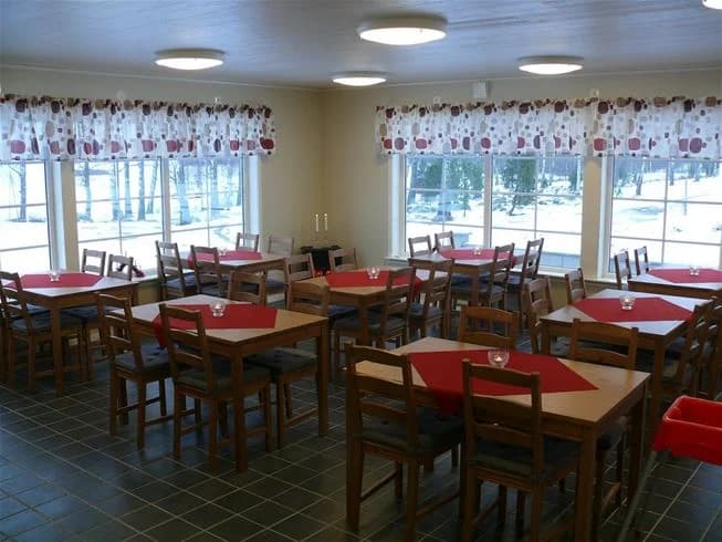 En gemytlig campingmiljö med ett träbord och stolar placerade på ett trägolv, i bakgrunden syns en cafeteria eller restaurangdel.