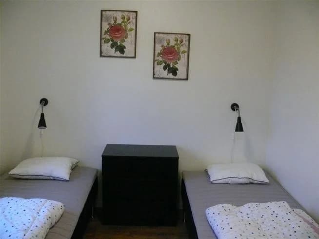 Ett enkelt och hemtrevligt sovrum med en dubbelsäng klädd i vita lakan. Golvet är av trä och väggarna är ljusa, vilket skapar en ljus och inbjudande atmosfär.