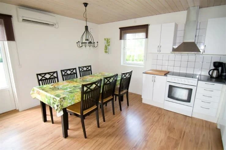 En interiörbild från Mjölknabbens camping som visar ett rymligt rum med trägolv och träpaneler i taket. Rummet är möblerat med ett matbord och stolar, vilket ger en hemtrevlig atmosfär.