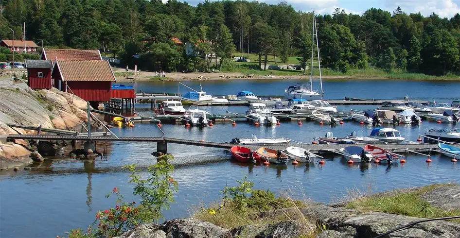 En bild av Lökholmens camping som visar ett vattendrag med flera båtar förtöjda vid strandkanten, omgiven av grönskande natur.