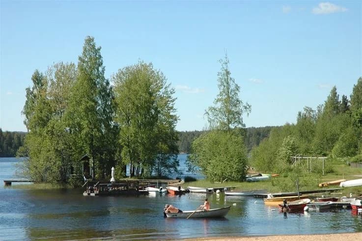 En lugn sjö med båtar förtöjda vid strandkanten, omgiven av grönskande träd vid Liens Camping.