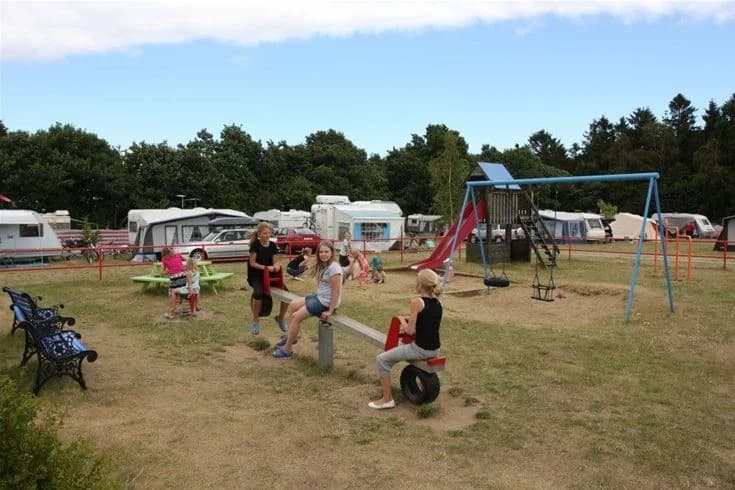 En familjevänlig campingplats med tält och husbilar, barn som leker i en park och en glädjefylld atmosfär vid Kiviks familjecamping.
