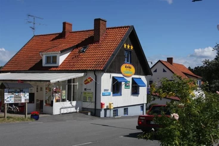 En campingplats med markis, flaggstång och en byggnad som har en skylt. Möjliga faciliteter inkluderar snabbmatsrestaurang och värdshus.