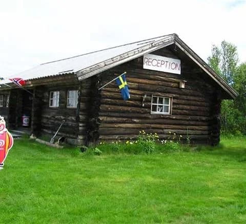 En timmerstuga med träpanel omgiven av en grön gräsmatta vid Karesuando camping & rekreation.