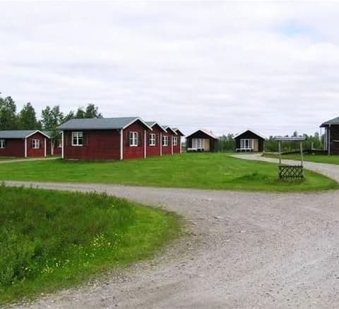 En gräsbevuxen campingplats med stugor i en lantlig miljö, omgiven av öppna fält i Karesuando.