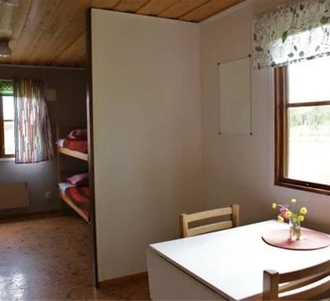 Ett varmt och inbjudande interiörfoto av ett rum på Karesuando camping & rekreation. Rummet har träpaneler på väggarna och taket, samt ett trägolv. Möblerna är enkla och funktionella, vilket skapar en rustik och avkopplande atmosfär.