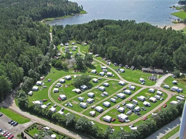 En fågelperspektiv av Jogersö Eco Camping vid kusten, omgiven av grönska och vatten. Den natursköna platsen inkluderar en bukt och är idealisk för friluftsliv och rekreation.