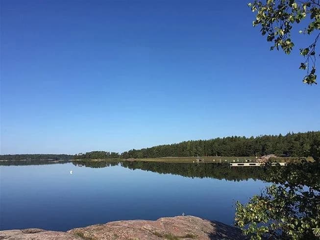 En klarblå himmel möter ett vidsträckt vattendrag, med en stilla sjö som sträcker sig mot horisonten vid Jogersö Eco Camping.