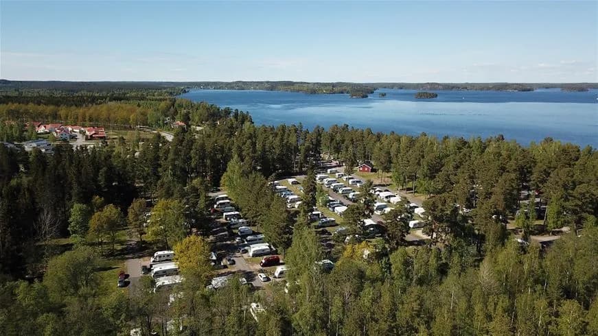 Flygbild av Hätte Camping med träd och kustområden. Bilden visar en kustlinje med en bukt som leder till sjölandskap, inramad av täta skogar och öppna ytor.
