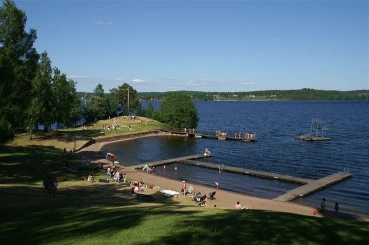 En sjö omgiven av grön natur vid Hätte Camping, där människor njuter av fritidsaktiviteter och avkopplande semesterstunder.