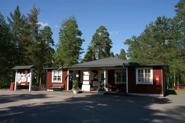 En solig dag på Hätte camping med gröna träd som ger skugga över en stuga och en tillhörande uteplats i stugområdet.
