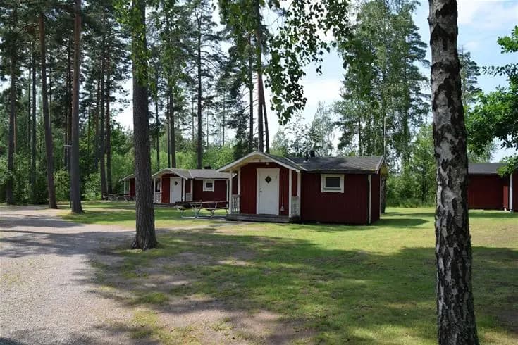 En landskapsbild av Hätte Camping med grönskande träd, gräs och stugor belägna i ett lantligt område.