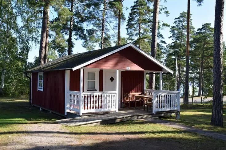 Bild av en charmig stuga med träfasad och tak, omgiven av grönska. Stugan har en liten veranda och ligger på Hätte camping, ett populärt besöksmål.