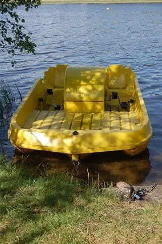 En uppblåsbar motorbåt ligger förtöjd vid strandkanten på Hjortsjöns camping, med klart vatten i bakgrunden.