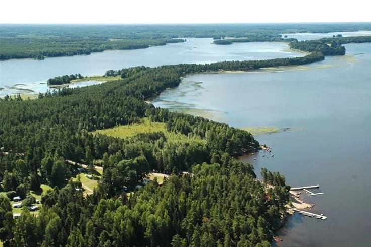 Flygbild över Hedesunda Camping med närliggande vattenresurser. Området visar en kustlinje med vattenvägar omgiven av grönska, vilket skapar en naturskön miljö för både camping och rekreation.