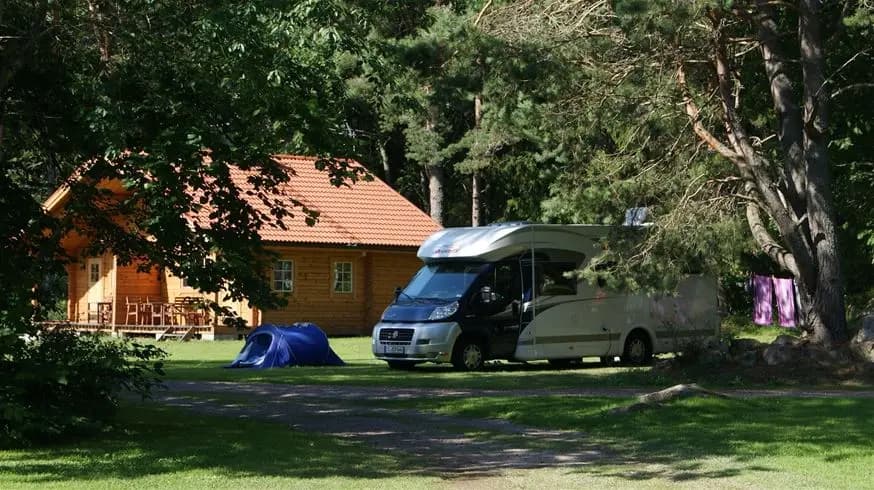 Alt-text: En vy över Hedesunda Camping med gräsfält, tält och husbilar omgivna av träd och trädgårdsbyggnader.