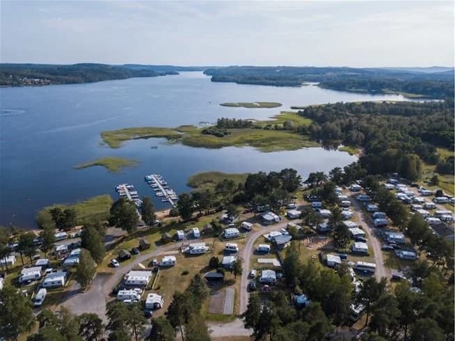 Vy över en naturskön sjö vid Hanatorps camping, med omgivande stränder och skogsbeklädda landformer i bakgrunden.