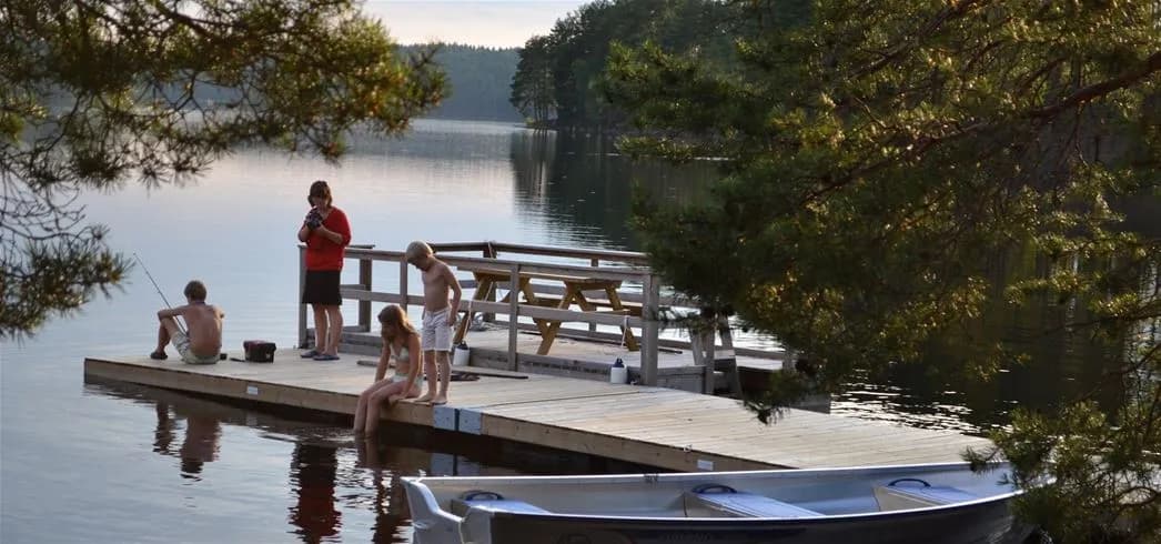 En naturskön vy över Sävsjön vid Grums Fish n' Camp, med klarblått vatten omgivet av grönskande träd och en fridfull strandlinje, perfekt för rekreation och avkoppling.