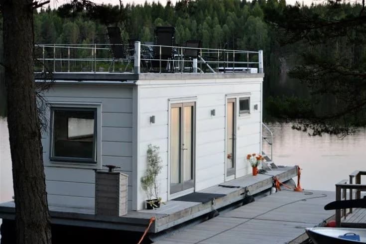 En sjö med flera båtar förtöjda vid en brygga, omgiven av grönskande natur och lugnt vatten vid Grums Fish n' Camp - Sävsjön.