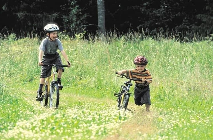 En cykel står parkerad med sitt gröna styre, omgiven av frodig natur och gräs på Glaskogens vildmarkscamping. En cykelhjälm är placerad ovanpå cykelns ram.