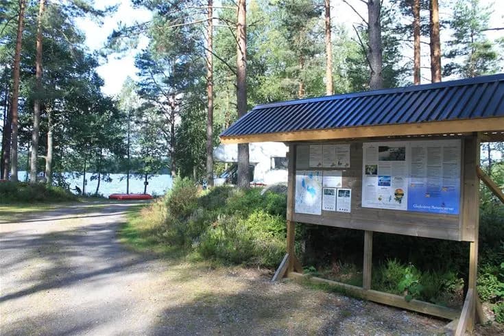 En vy över Glaskogens vildmarkscamping med en stor sjö omgiven av tät skog i bakgrunden, vilket skapar en fridfull och naturnära atmosfär.