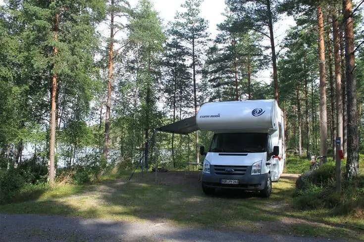 En campingplats med husbilar och husvagnar uppställda i det natursköna Glaskogen, omgiven av skogslandskap.