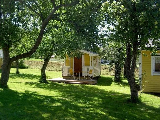 En mysig stuga omgiven av en prunkande trädgård med grönskande gräsmatta. Perfekt för en avkopplande stund i naturen med tillgång till park och skuggiga omgivningar.