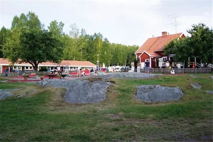 En öppen grön plats vid Frykenbadens camping, med gräsmatta, picknickbord och utomhusmöbler för rekreation och avkoppling.