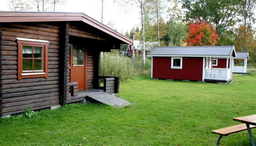 En charmig trästuga vid Emmaboda camping omgiven av grönska, med en enkel dörr och träpanel.