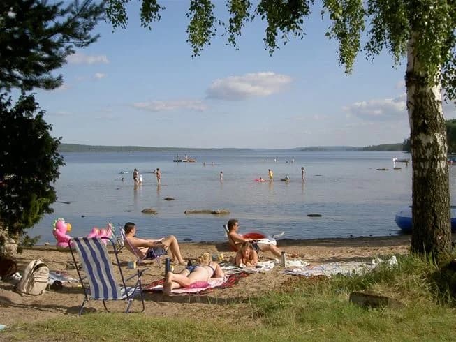 En naturskön campingplats vid en sjö, med en sandstrand och grönska runtomkring. Perfekt för rekreation och semester.