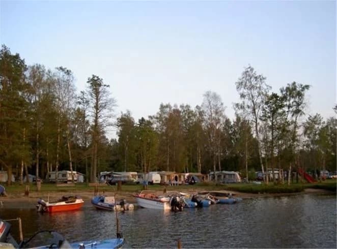 En bild av E4:ans camping som visar en vattenväg med båtar, en strandkant, en sjö och en marina synliga i bakgrunden. Detta är ett populärt rekreationsområde för båtliv och naturskön avkoppling.