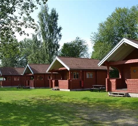 Bild av Djupadalsbadet bad och camping, som visar gröna gräsmattor och trädgårdsbyggnader omgivna av lummiga landskap. En asfalterad uppfart leder genom området, vilket ger en inbjudande atmosfär för besökare.