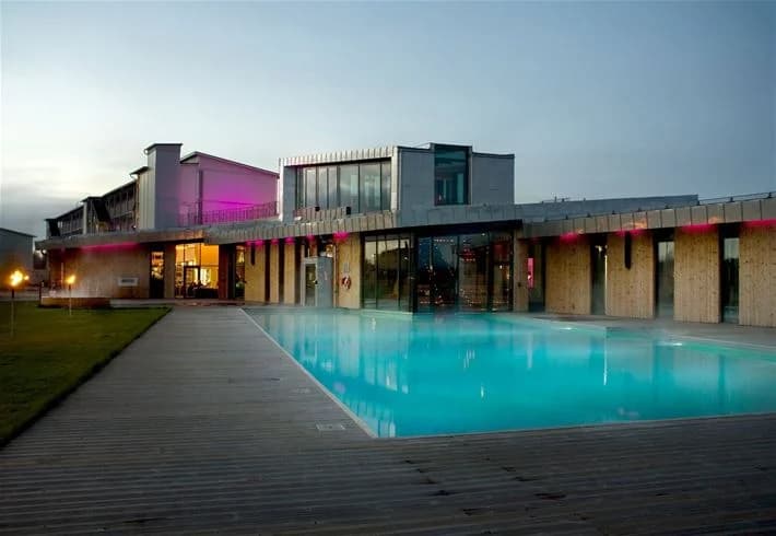 Alt-text: En upplyst pool på Cape East resort, omgiven av moderna byggnader och natursköna omgivningar, fångad vid nattid.