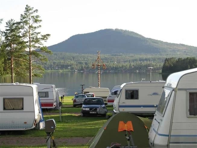 En husbil parkerad vid en naturskön sjö i Lake District, omgiven av grönskande skog och berg i bakgrunden. Solen skiner över den idylliska campingplatsen vid sjökanten.