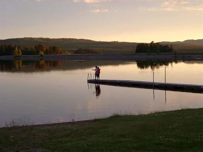 En pittoresk vy vid Sollerö Camping med spegelklart vatten, grönskande strandkanter och en klar blå himmel.